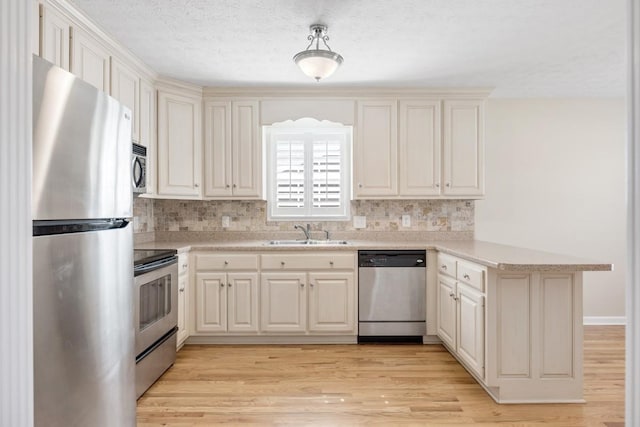 kitchen featuring stainless steel appliances, a peninsula, a sink, light wood-style floors, and light countertops