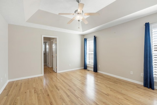 unfurnished room featuring light wood-style floors, a tray ceiling, baseboards, and a ceiling fan