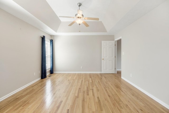 spare room featuring light wood-type flooring, baseboards, and a tray ceiling