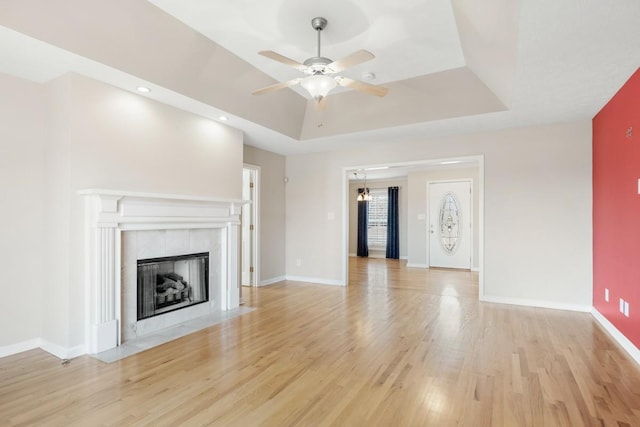 unfurnished living room with light wood-style floors, a fireplace, baseboards, and a raised ceiling