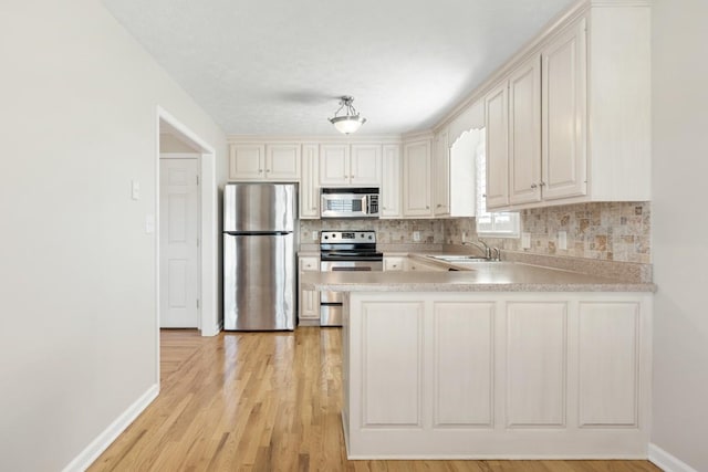 kitchen with light wood-style flooring, stainless steel appliances, a peninsula, light countertops, and decorative backsplash