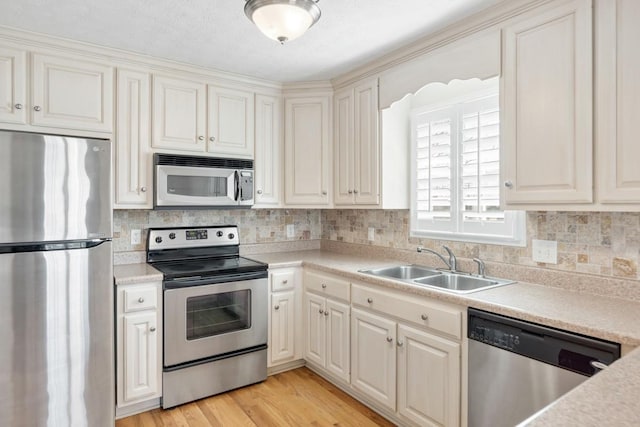 kitchen featuring light wood finished floors, tasteful backsplash, appliances with stainless steel finishes, and a sink