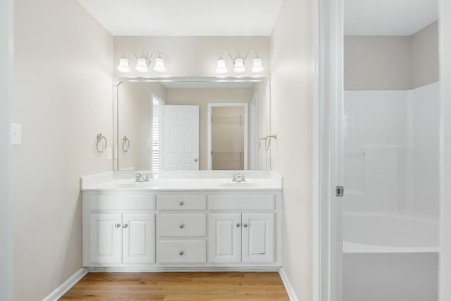 full bathroom with double vanity, baseboards, a sink, and wood finished floors