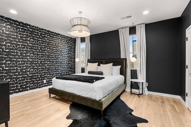 bedroom with visible vents, an accent wall, wood finished floors, baseboards, and wallpapered walls