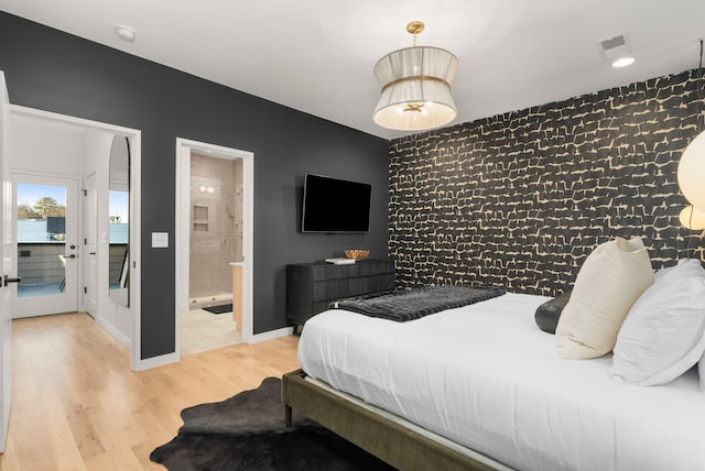 bedroom featuring visible vents, baseboards, connected bathroom, light wood-style flooring, and an accent wall