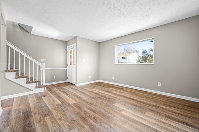 spare room featuring baseboards, a textured ceiling, stairway, and wood finished floors