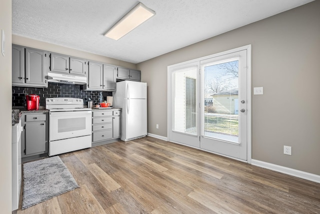 kitchen with white appliances, tasteful backsplash, light wood-style flooring, gray cabinetry, and under cabinet range hood