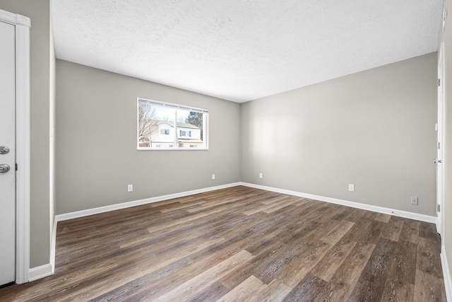 empty room with a textured ceiling, dark wood finished floors, and baseboards