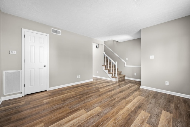 unfurnished room featuring stairway, wood finished floors, visible vents, and baseboards