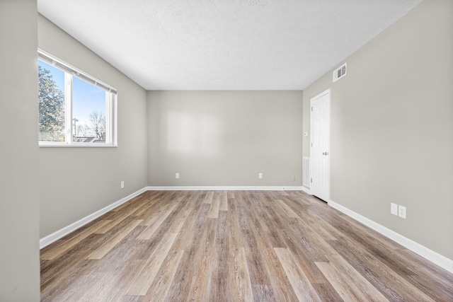 spare room with light wood-type flooring, visible vents, a textured ceiling, and baseboards