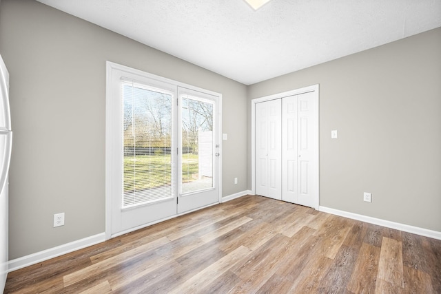 unfurnished bedroom with a closet, a textured ceiling, baseboards, and wood finished floors