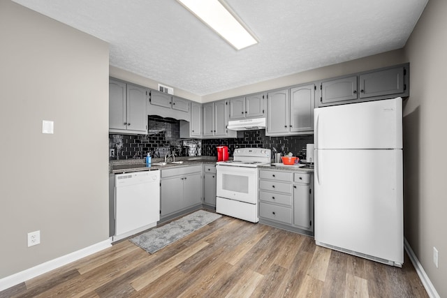 kitchen featuring tasteful backsplash, white appliances, light wood-style flooring, and under cabinet range hood