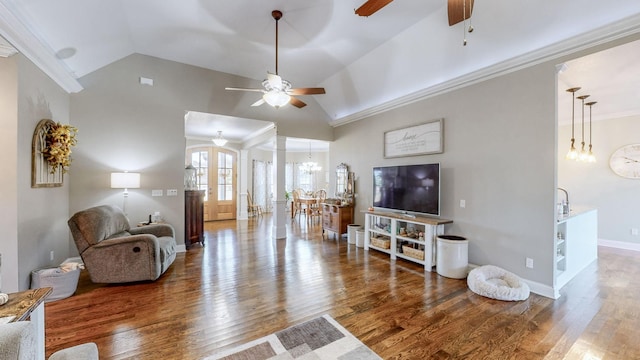 living room with baseboards, lofted ceiling, ornamental molding, wood finished floors, and ceiling fan with notable chandelier