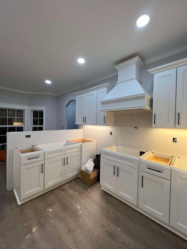 kitchen with arched walkways, custom range hood, dark wood-type flooring, crown molding, and recessed lighting