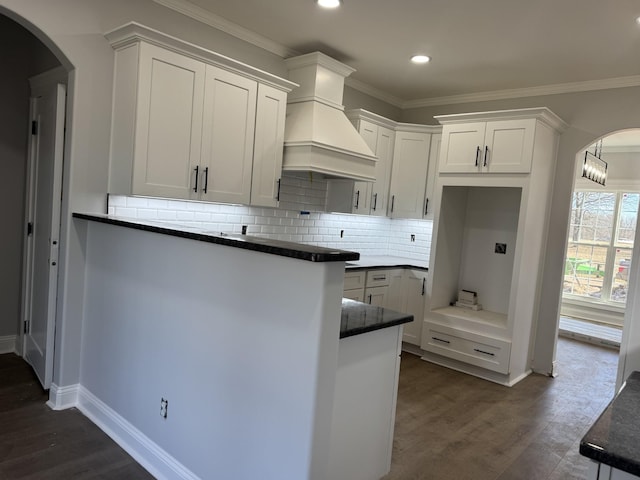 kitchen with dark wood-style floors, arched walkways, custom range hood, and white cabinetry