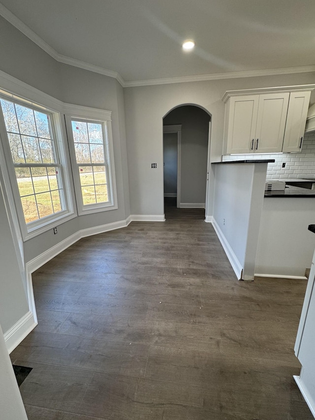 interior space with arched walkways, ornamental molding, dark wood finished floors, and baseboards