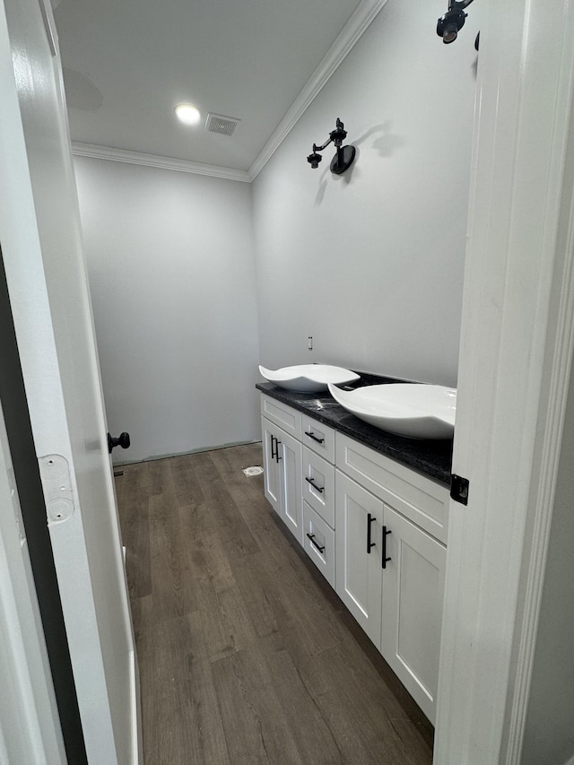 bathroom with a sink, wood finished floors, visible vents, double vanity, and crown molding