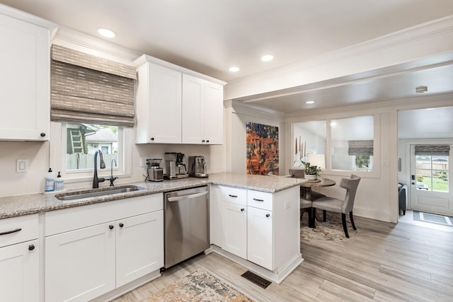 kitchen featuring light wood finished floors, stainless steel dishwasher, a sink, and white cabinetry