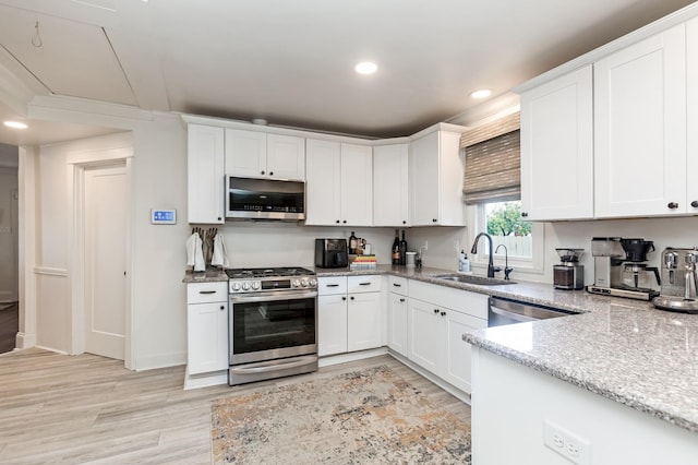 kitchen featuring light stone counters, appliances with stainless steel finishes, a sink, and white cabinetry