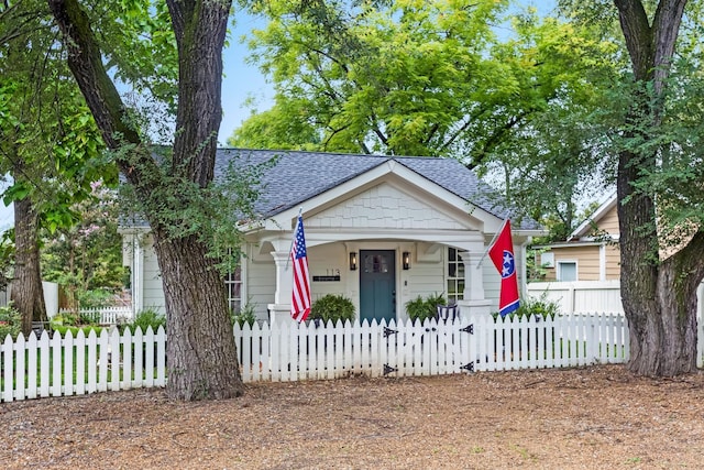 bungalow with a fenced front yard, a porch, and a shingled roof