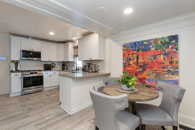 kitchen with stainless steel appliances, visible vents, white cabinets, a sink, and a peninsula