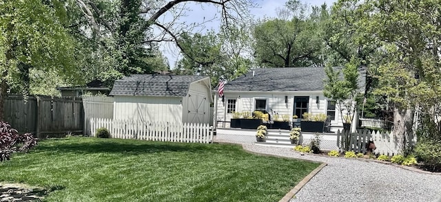 exterior space featuring a fenced backyard, a shingled roof, an outdoor structure, a shed, and a front lawn