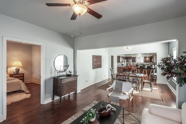 living area featuring baseboards, wood finished floors, and ceiling fan with notable chandelier