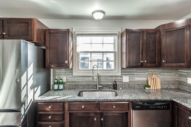 kitchen featuring a sink, tasteful backsplash, stainless steel appliances, dark brown cabinetry, and light stone countertops