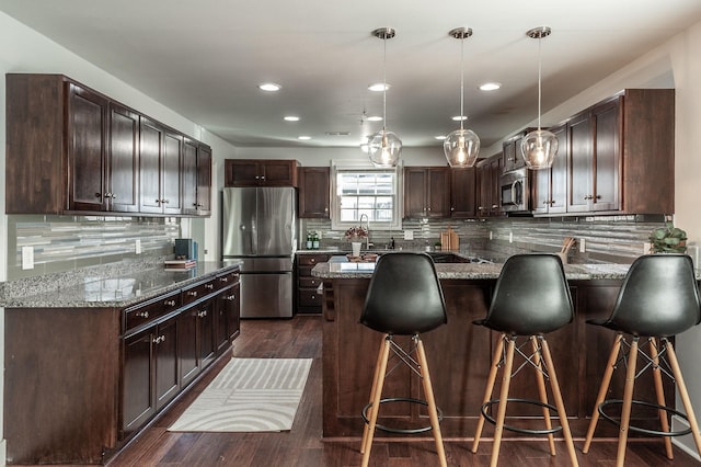 kitchen with stone countertops, dark brown cabinetry, appliances with stainless steel finishes, a peninsula, and dark wood-style flooring