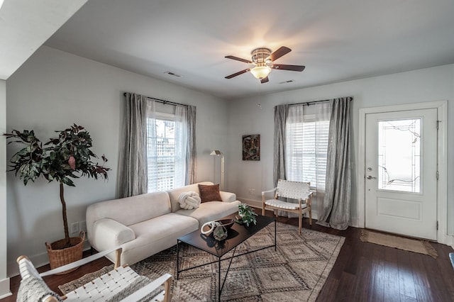 living area featuring dark wood-type flooring, a ceiling fan, visible vents, and baseboards