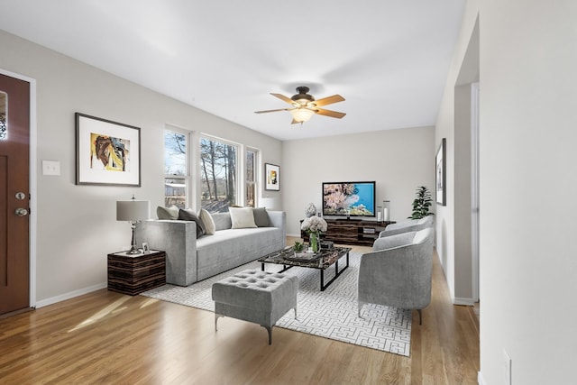 living area with baseboards, light wood-style flooring, and a ceiling fan