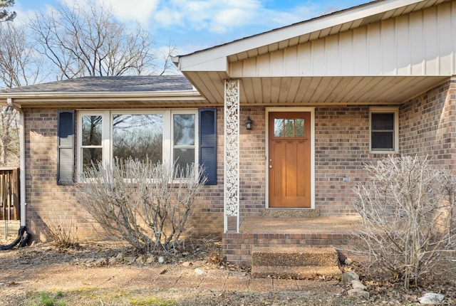 doorway to property featuring brick siding and a shingled roof