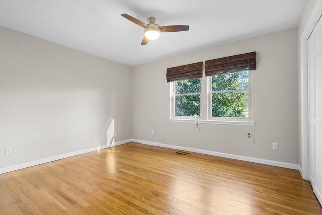 empty room with visible vents, light wood finished floors, a ceiling fan, and baseboards