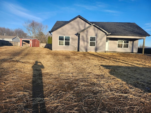 view of front of house featuring a shingled roof, an outbuilding, and fence