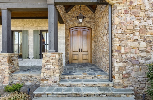 property entrance with stone siding, brick siding, and covered porch