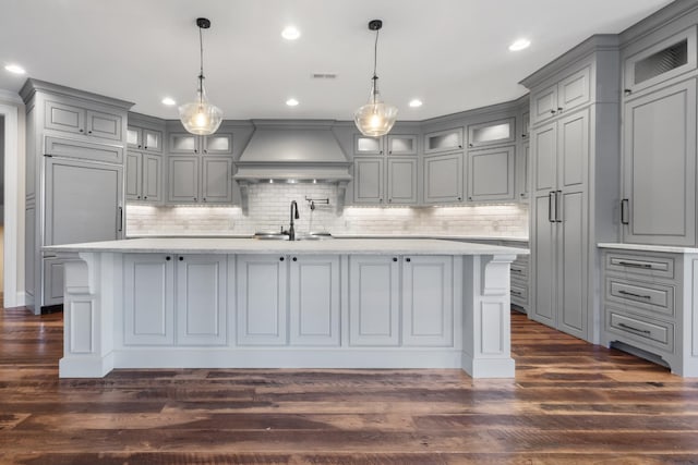 kitchen featuring backsplash, a center island with sink, gray cabinets, and custom range hood