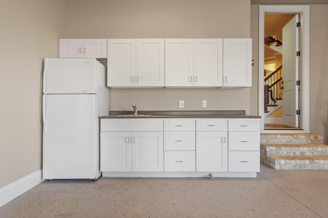 kitchen with a sink, white cabinetry, dark countertops, and freestanding refrigerator