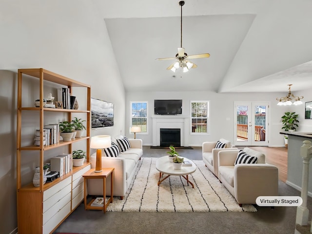 living room featuring a fireplace, high vaulted ceiling, wood finished floors, and ceiling fan with notable chandelier