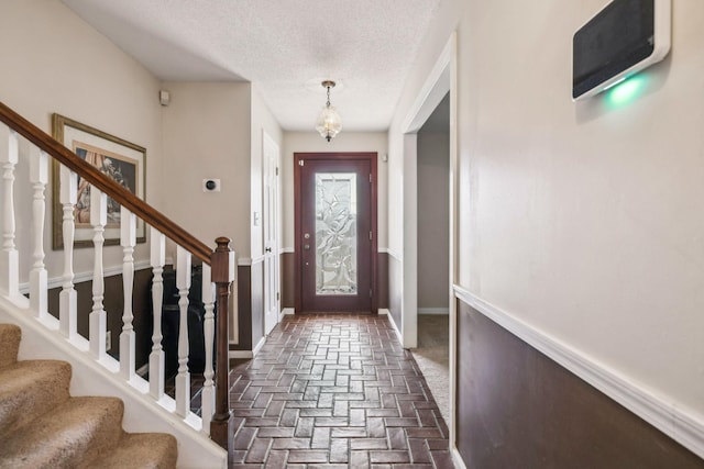 entryway with a textured ceiling, stairway, brick floor, and baseboards