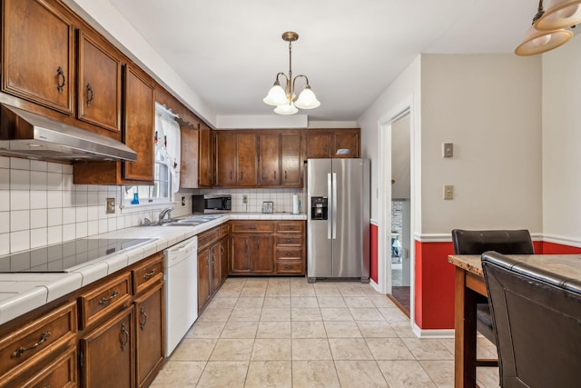 kitchen with a notable chandelier, under cabinet range hood, stainless steel appliances, a sink, and tile counters