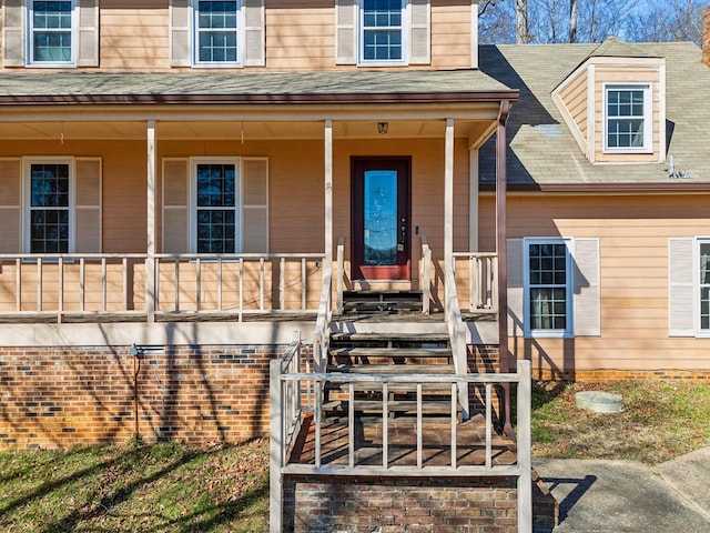 view of exterior entry with covered porch and a shingled roof