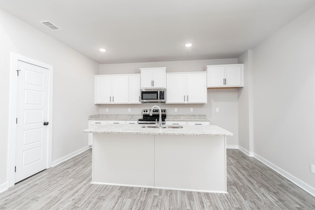 kitchen with stainless steel appliances, visible vents, white cabinets, a sink, and an island with sink