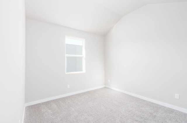 empty room featuring carpet flooring, vaulted ceiling, and baseboards