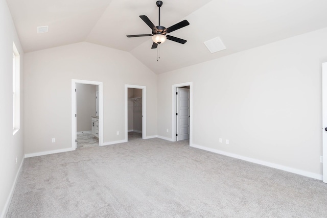 unfurnished bedroom with a walk in closet, ensuite bathroom, light carpet, vaulted ceiling, and baseboards