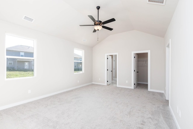 unfurnished bedroom with a walk in closet, lofted ceiling, light colored carpet, visible vents, and baseboards