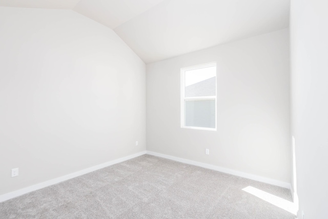 carpeted empty room with vaulted ceiling and baseboards