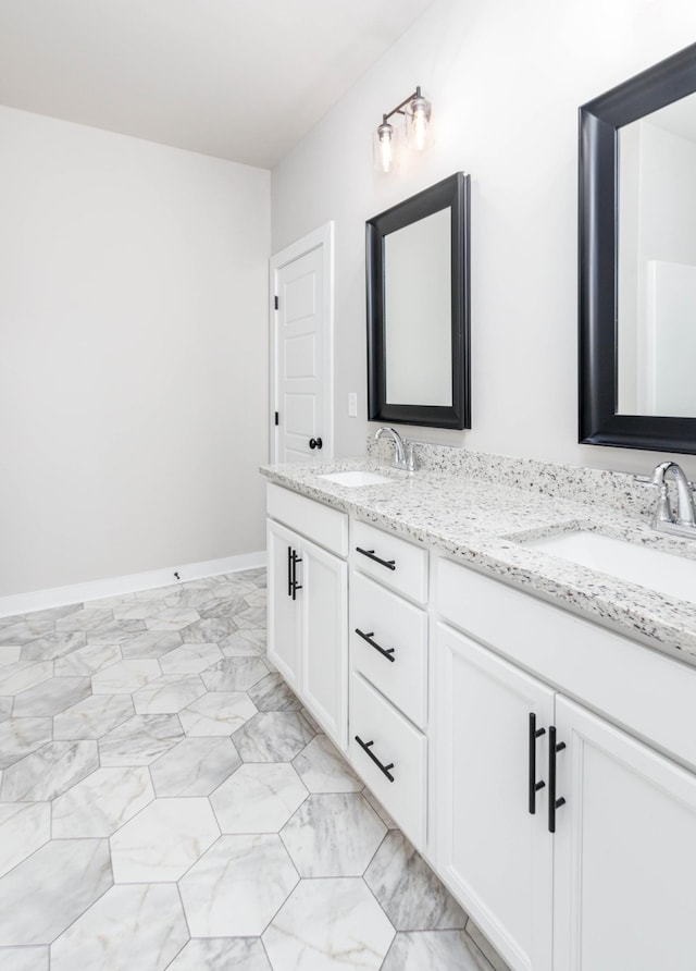 full bath featuring marble finish floor, a sink, baseboards, and double vanity