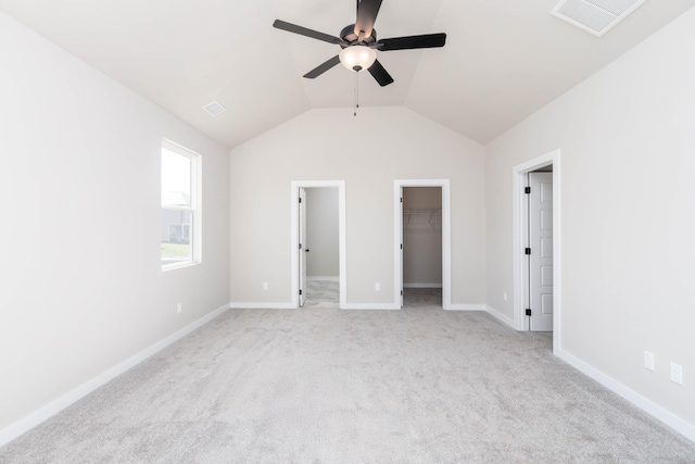 unfurnished bedroom featuring a walk in closet, lofted ceiling, visible vents, light carpet, and baseboards