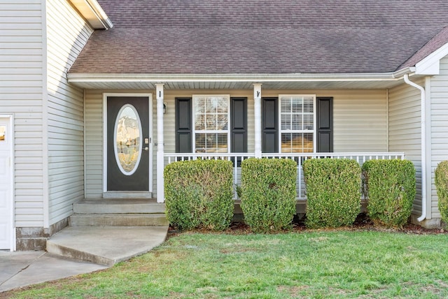 view of exterior entry featuring a garage, a shingled roof, a lawn, and a porch