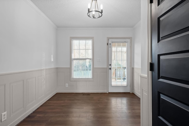 doorway to outside with dark wood finished floors, a wainscoted wall, ornamental molding, an inviting chandelier, and a textured ceiling